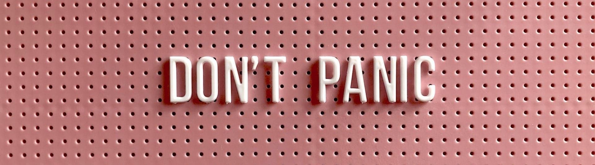 White plastic letters on a pink pegboard spelling DON'T PANIC.